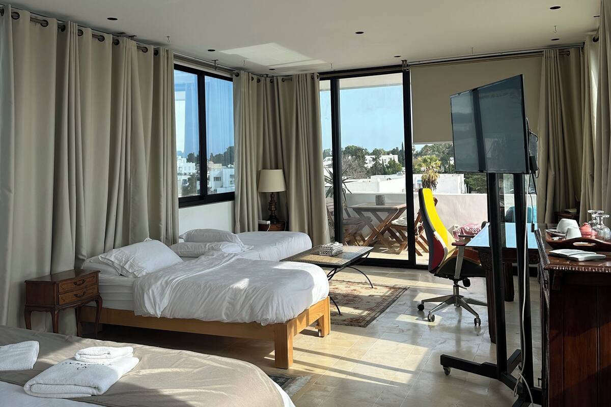 Una habitación de hotel con dos camas, un escritorio con computadora, una silla y un televisor.