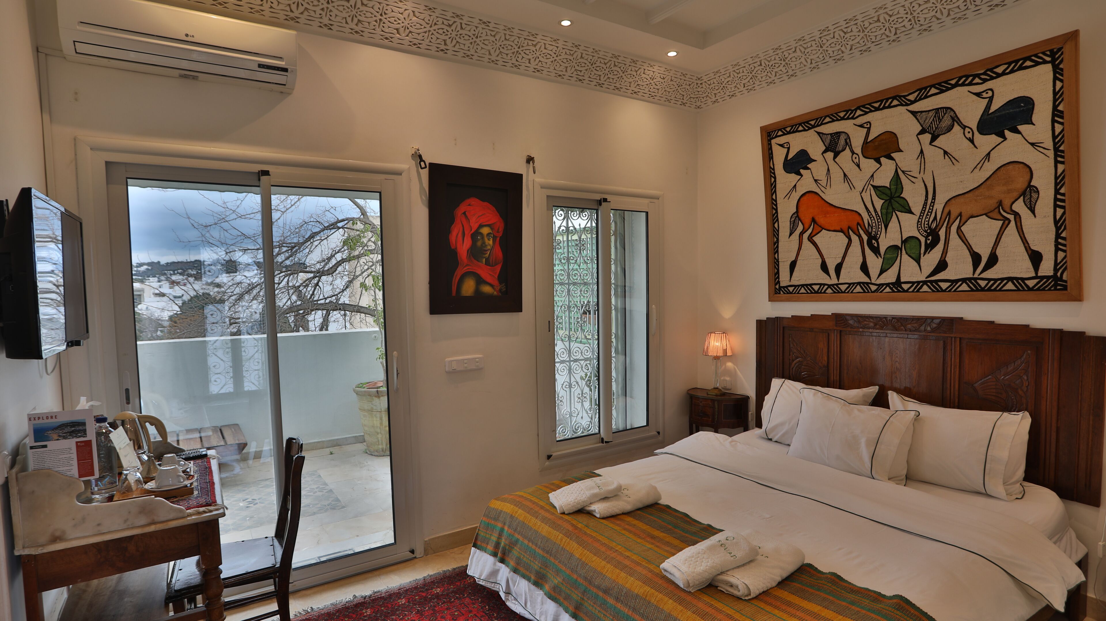 A hotel room with a bed, a TV, a window with a view of trees, and a painting on the wall.