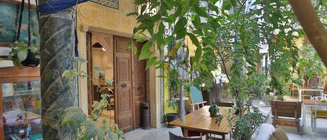 An outdoor seating area with a wooden table and chairs, surrounded by potted plants and a decorative column.