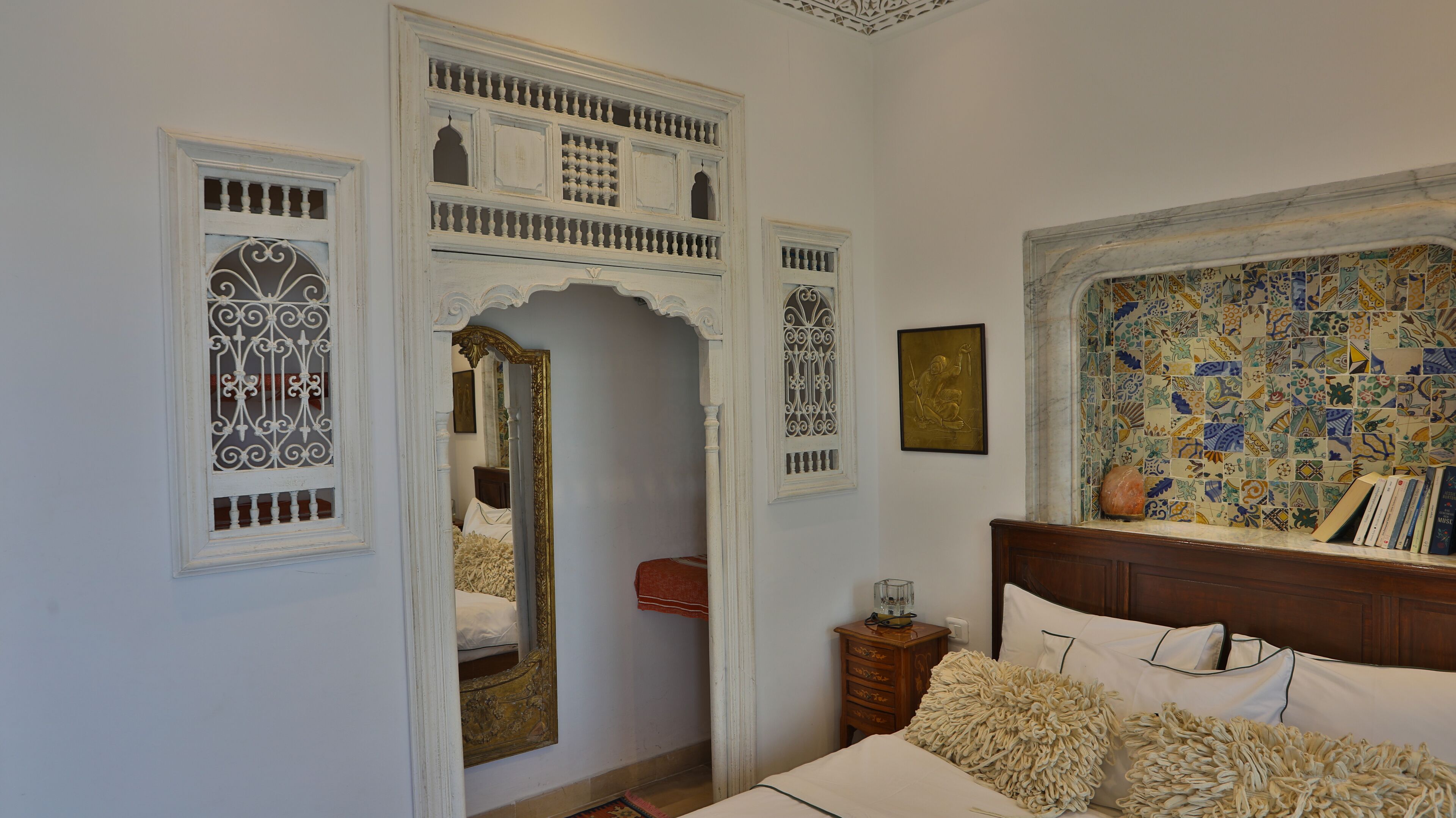 Un dormitorio con una cama, una mesita de noche de madera, un espejo y una pared con azulejos estampados.