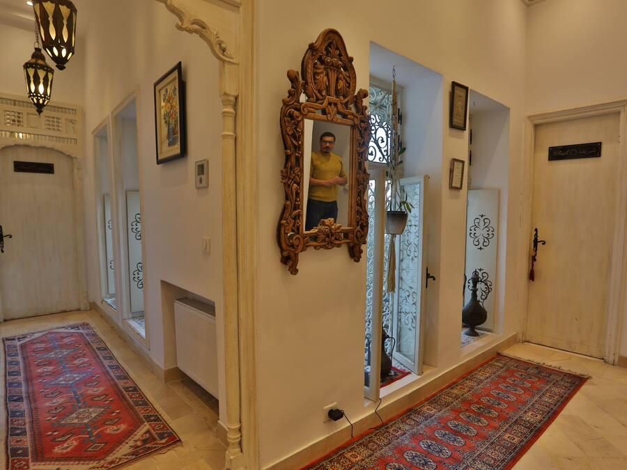 Un pasillo con puertas de madera ornamentadas, un espejo grande y alfombras estampadas.