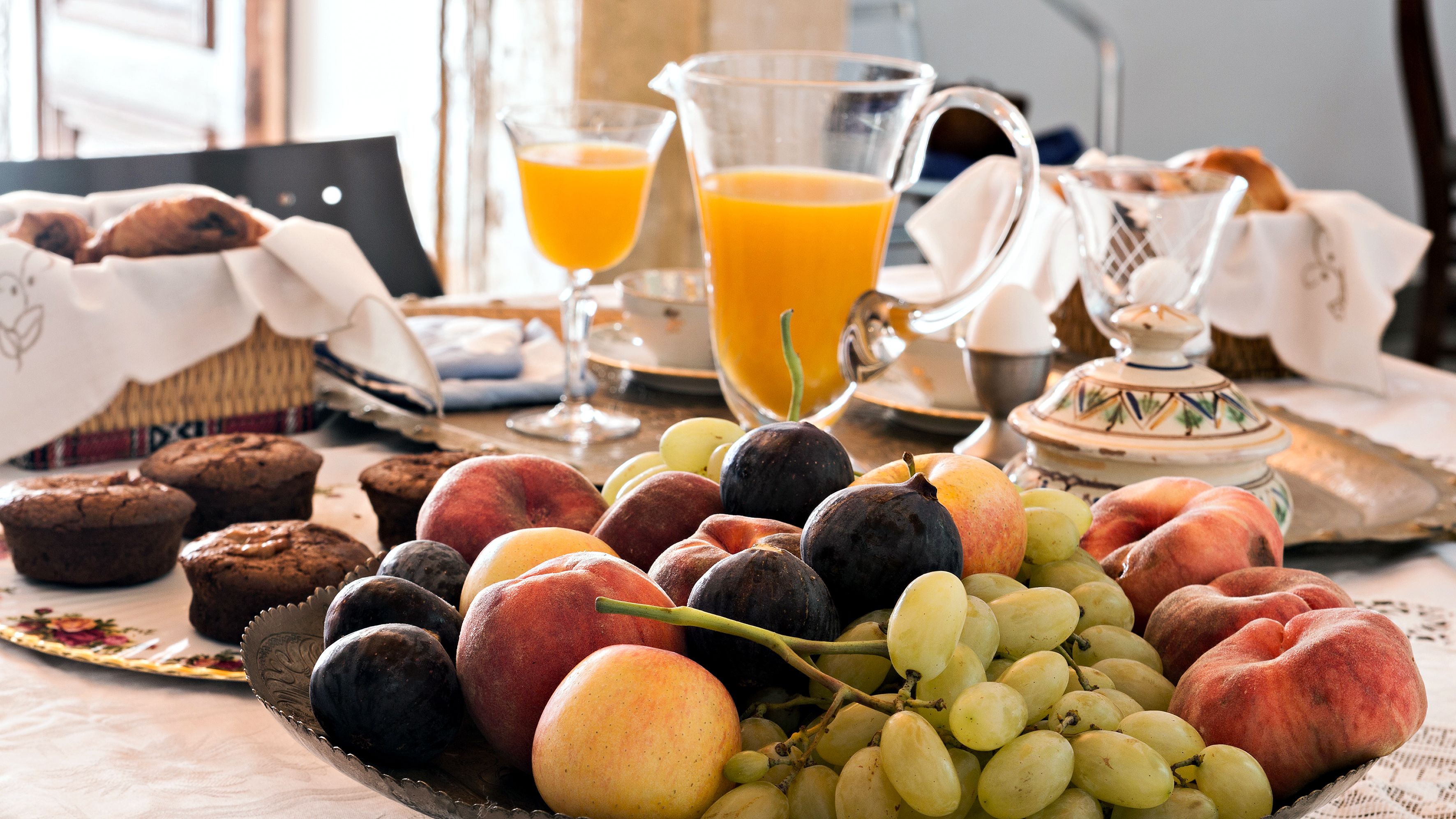 Una mesa de desayuno con pasteles, frutas y una jarra de jugo de naranja.