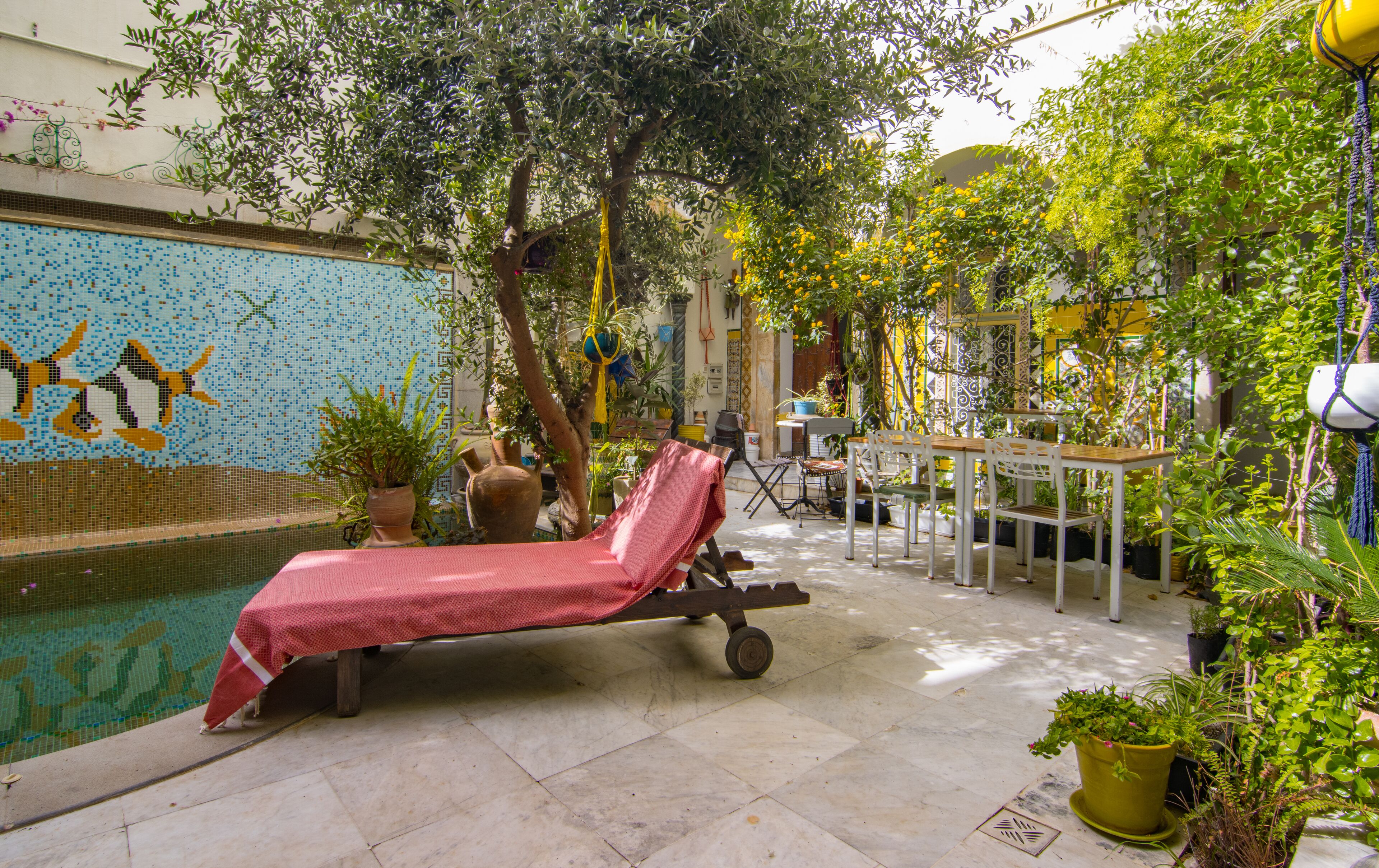 A poolside area with a lounge chair, potted plants, and a tiled wall with a mosaic design.