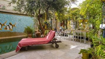 A poolside area with a lounge chair, potted plants, and a tiled wall with a mosaic design.