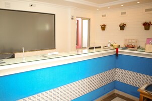 Un área de recepción con una paleta de colores azul y blanco, un televisor de pantalla plana grande, un mostrador de recepción y una cesta con flores sujeta a la pared.