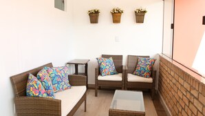 A balcony with wicker furniture, including a sofa and chairs, and a small table. There are three wicker baskets with flowers on the wall above the furniture. - Hotel Açoriano (Penha)