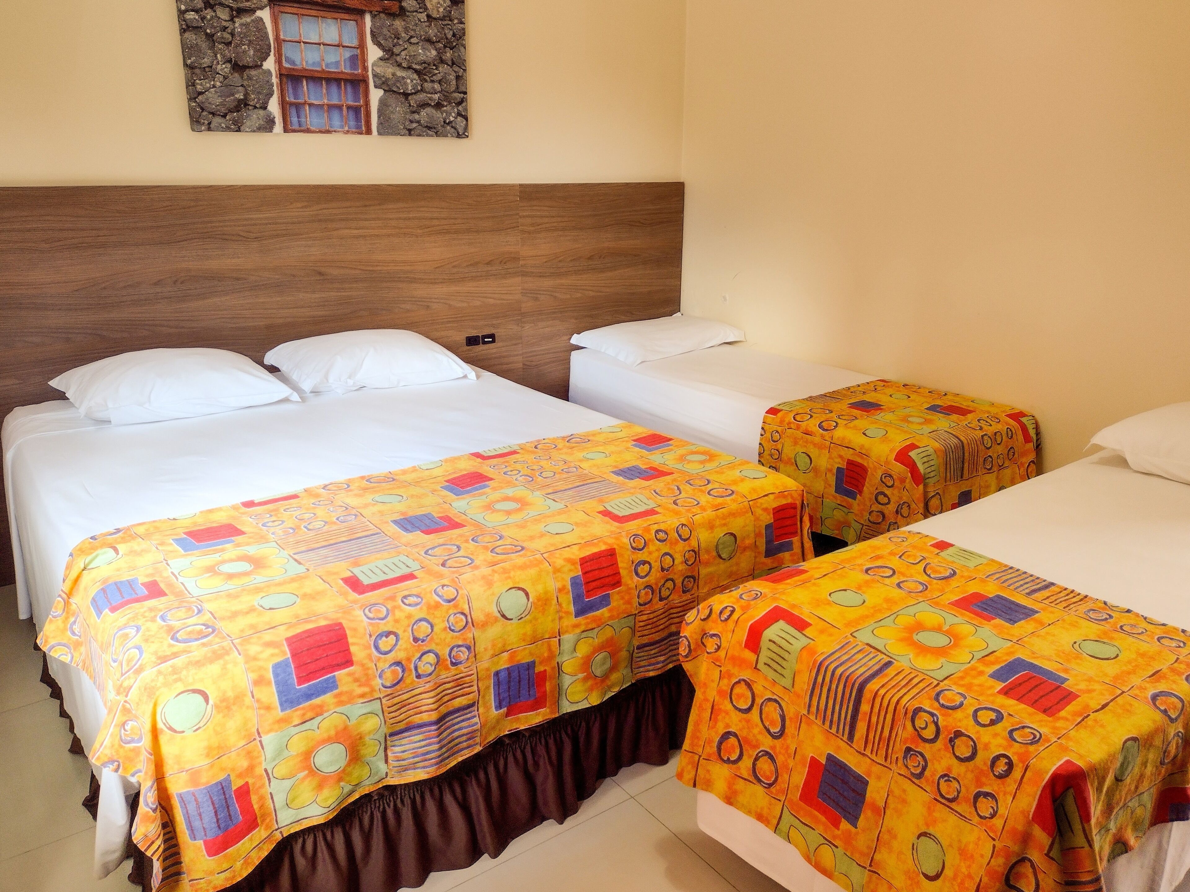 A hotel room with two single beds and a double bed, each with white linens and colorful bedspreads.