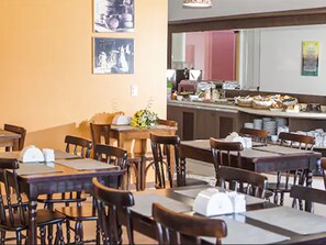 Un espace repas comprenant plusieurs tables et chaises, un comptoir où sont exposés des produits alimentaires, et un mur orné de tableaux.