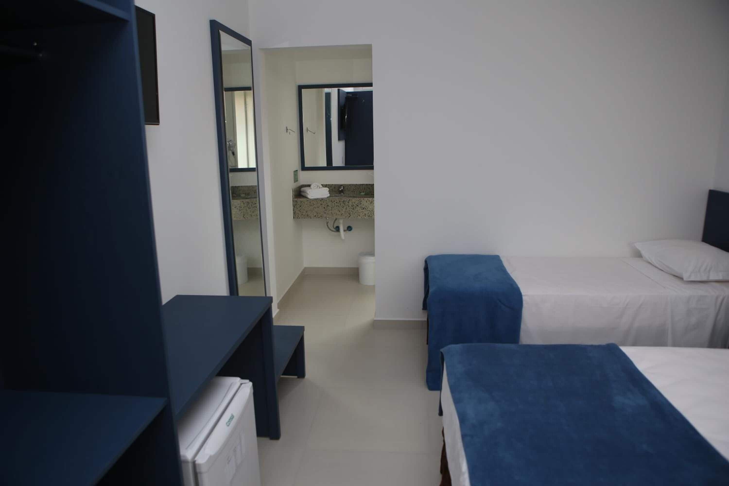Een hotelkamer met twee bedden, een bureau, een spiegel en een badkamer met wastafel en toilet.