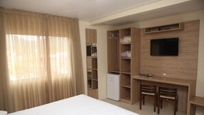 A hotel room with a bed, a desk with two chairs, a TV mounted on the wall, and a wardrobe with shelves. - Hotel Açoriano (Penha)