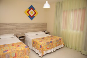Una habitación de hotel con dos camas, un cabecero de madera, una mesita de noche, un teléfono y una decoración de pared geométrica y colorida.