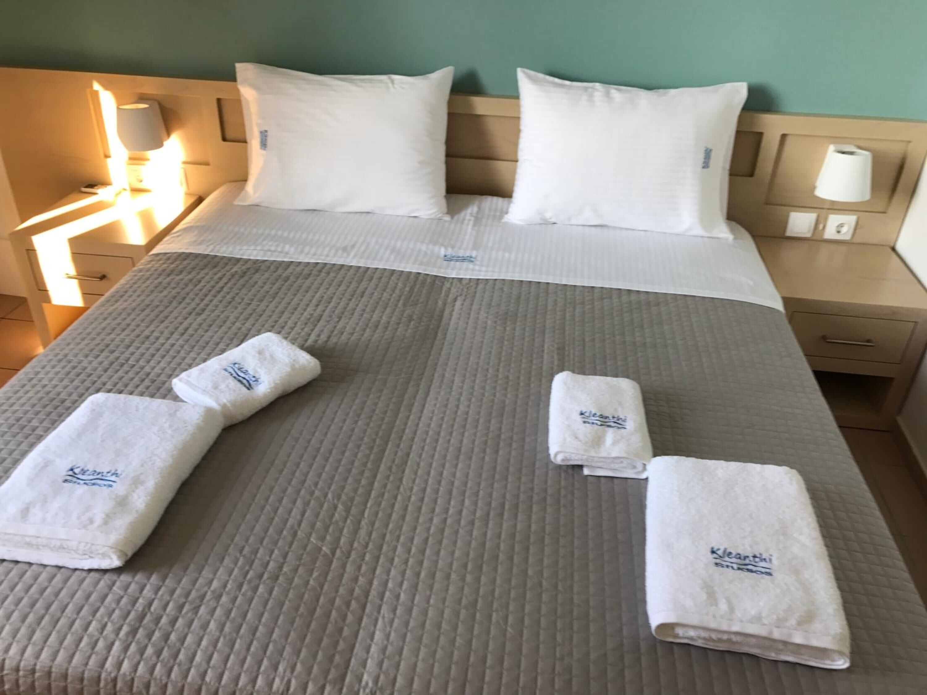 Una cama bien hecha con sábanas blancas, dos almohadas y tres toallas dobladas con un logotipo.
