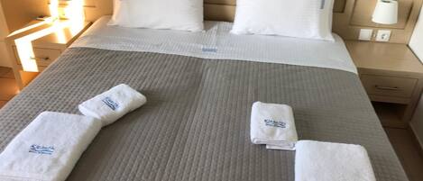 Una cama bien hecha con sábanas blancas, dos almohadas y tres toallas dobladas con un logotipo.