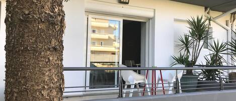 Un balcón con barandilla, un árbol y la entrada de un edificio.
