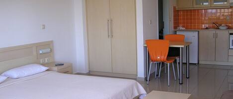 A hotel room with a bed, a desk, an orange chair, and a kitchenette.