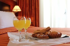 Ein Bett mit weißer Bettdecke, zwei Orangensaftgläser und ein Tablett mit Gebäck.