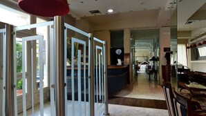 Eine Hotelhalle mit einer Rezeption, einer Wartezone mit Stühlen und Tischen sowie einer Glastür zum Ausgang.