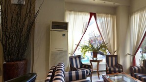 Ein Hotelzimmer mit gestreiften Sesseln, einer Couch, einer Topfpflanze und einer großen Klimaanlage.