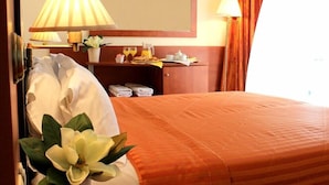 Ein Hotelzimmer mit einem Bett, einem Nachttisch mit Lampe, einem Spiegel, einem kleinen Tisch mit Frühstücksangebot und einem Fenster mit Vorhängen.