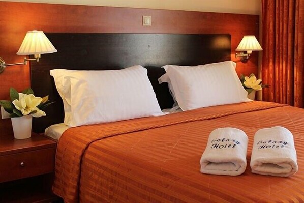 Ein Hotelzimmer mit einem großen Bett, zwei Kissen, einem Nachttisch mit Lampe und einer Vase mit Blumen.