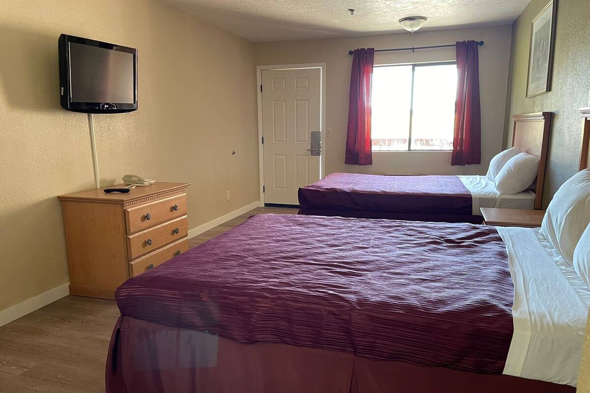 Quarto com duas camas, cómoda, televisão e janela com cortinas.