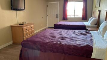 Un dormitorio con dos camas, un aparador, un televisor y una ventana con cortinas.
