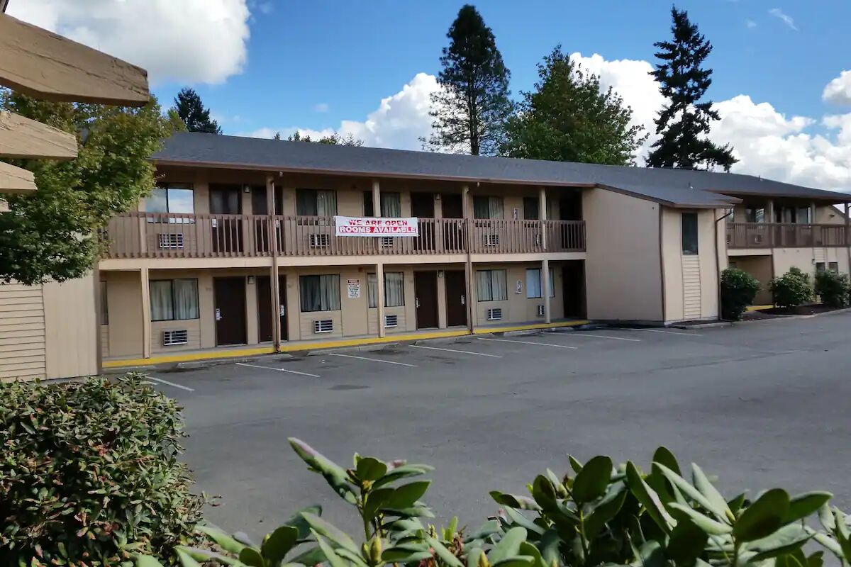 Un motel avec un panneau indiquant qu’il y a des chambres disponibles. Il comporte plusieurs étages avec des balcons et un parking à l’avant.