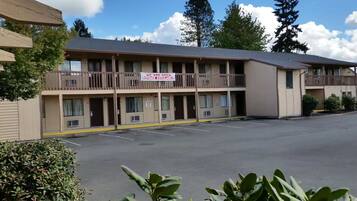 A motel with a sign indicating availability. It has multiple floors with balconies and a parking lot in front.