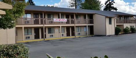 Un motel avec un panneau indiquant qu’il y a des chambres disponibles. Il comporte plusieurs étages avec des balcons et un parking à l’avant.