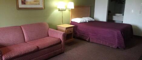 Una habitación de hotel con un sofá rojo estampado, una cama con colcha morada, una mesita de noche con dos lámparas y un cuadro en la pared.