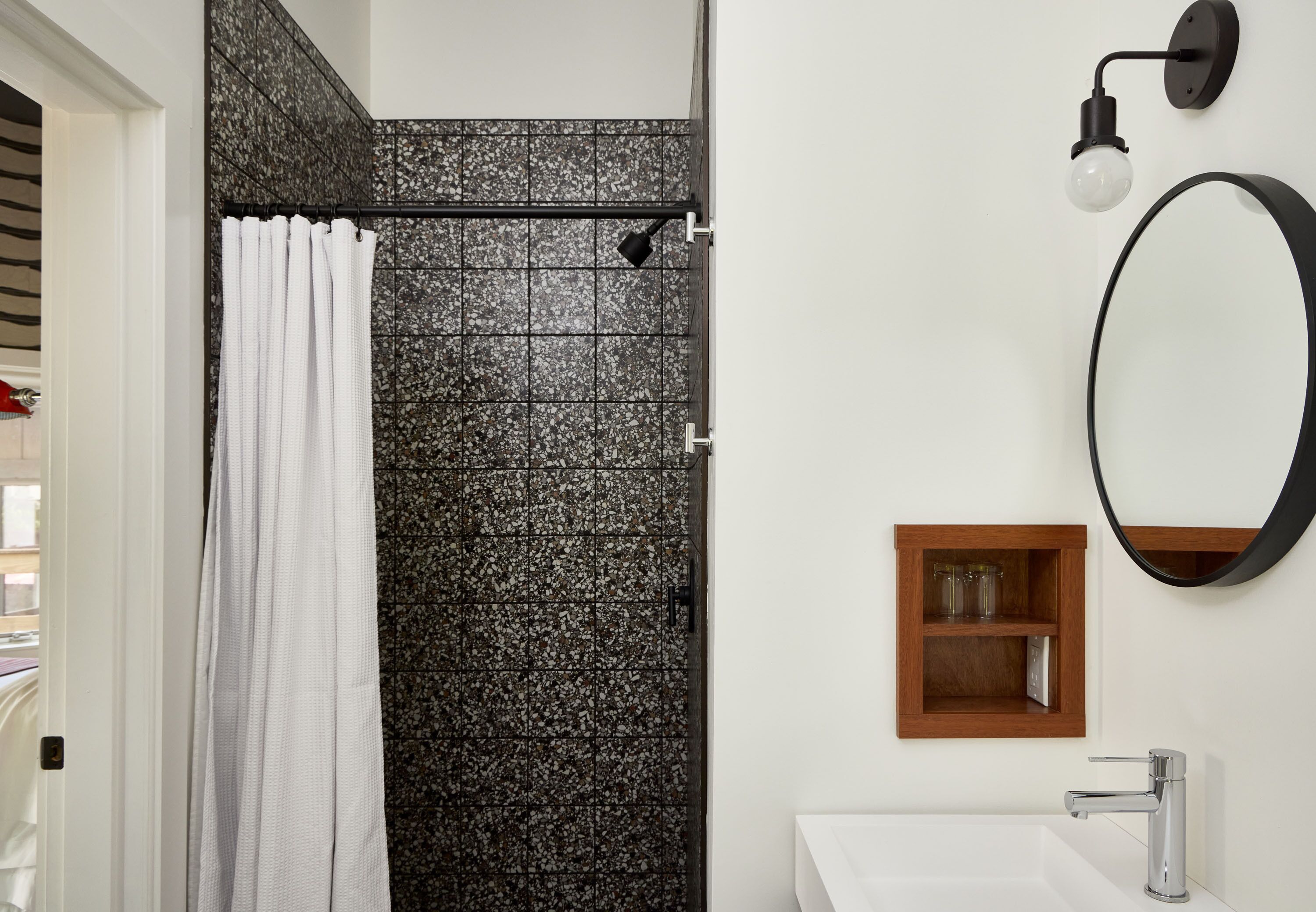 A bathroom with a shower, a sink, a mirror, and a shelf with glassware.