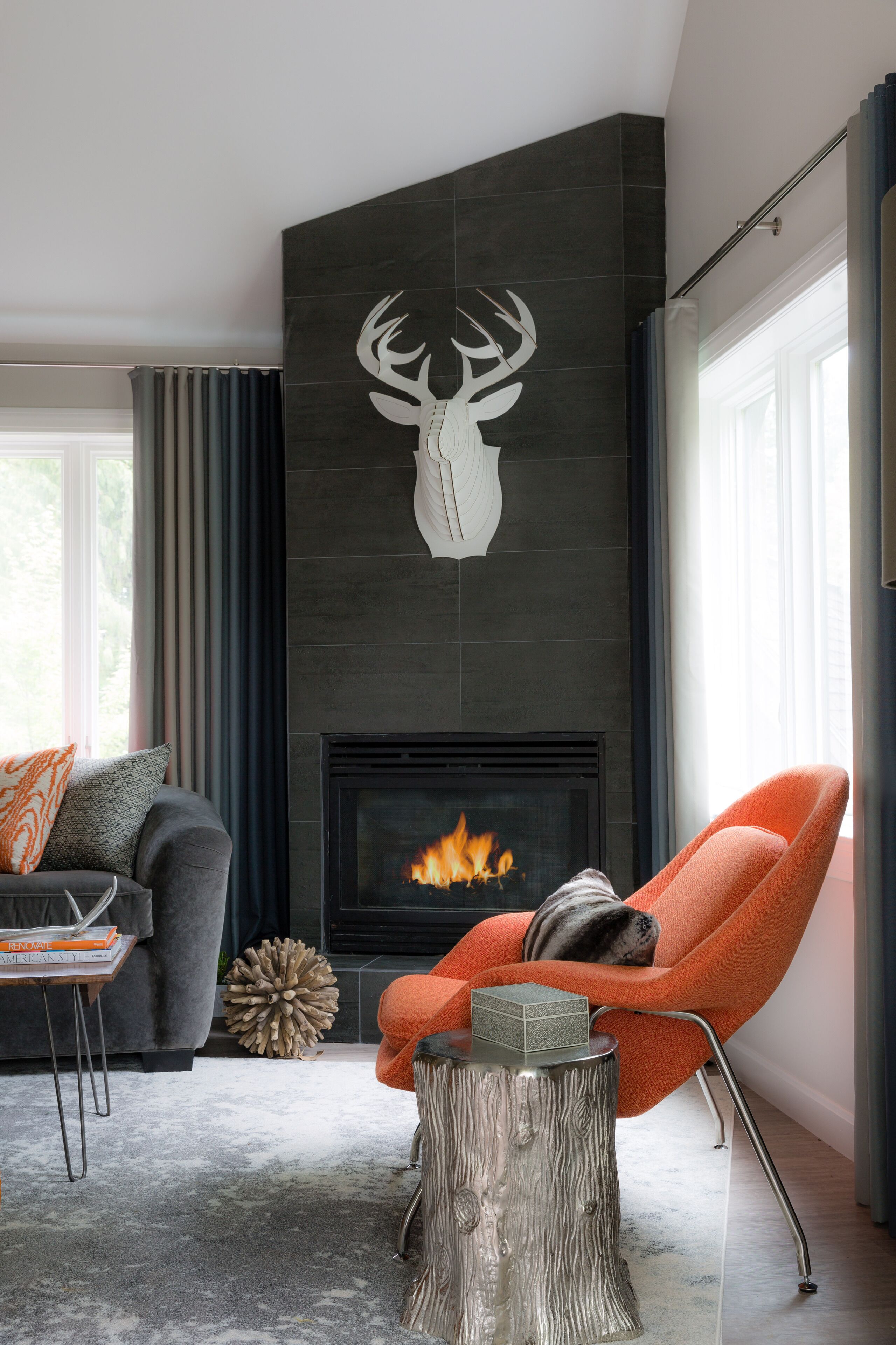 A modern living room with a fireplace, a sofa, an orange armchair, and a decorative deer head on the wall.