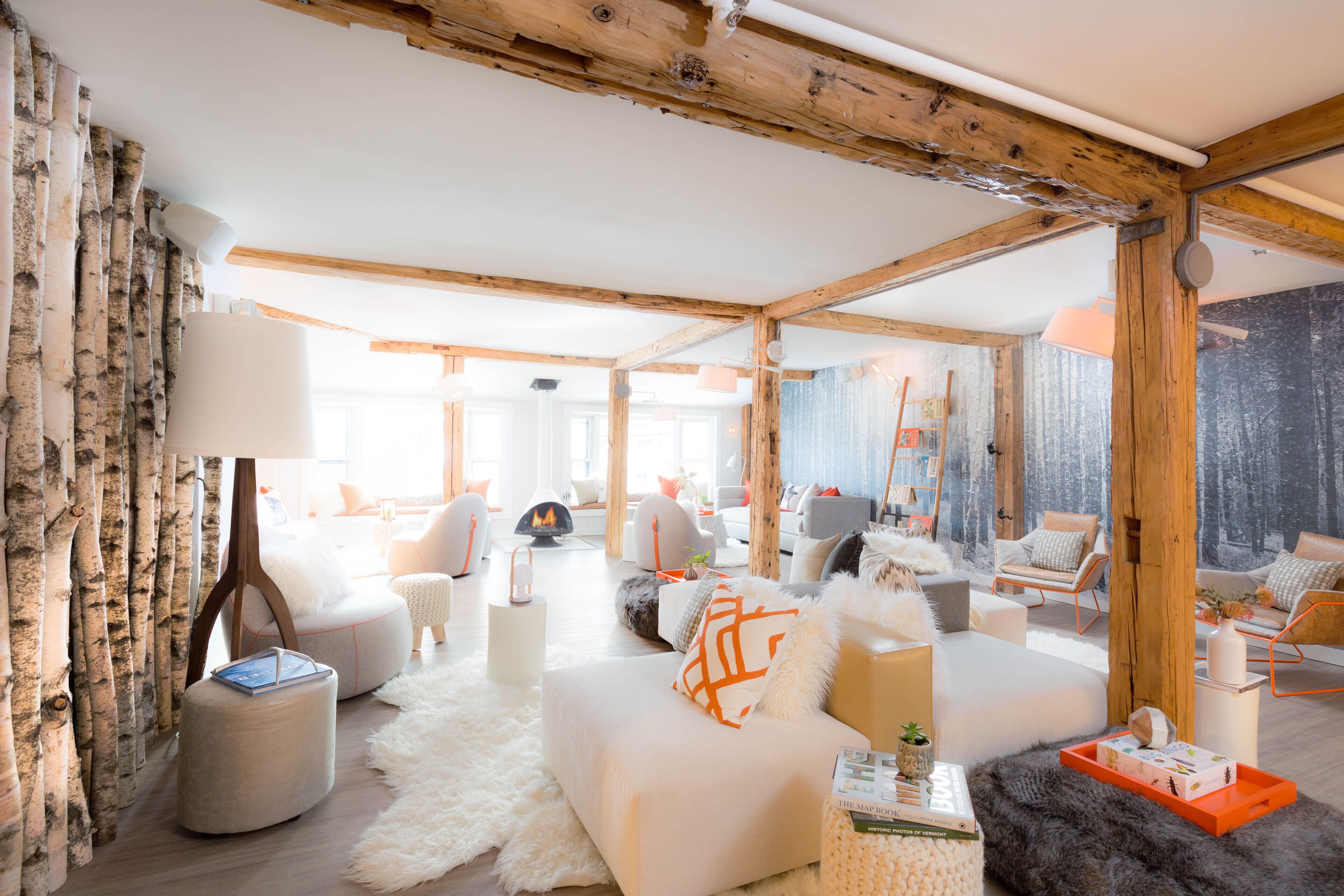 Un vaste salon doté d’un haut plafond, de poutres en bois et d’une grande fenêtre. On y trouve plusieurs coins salon, dont un canapé et des fauteuils, ainsi qu’une cheminée.