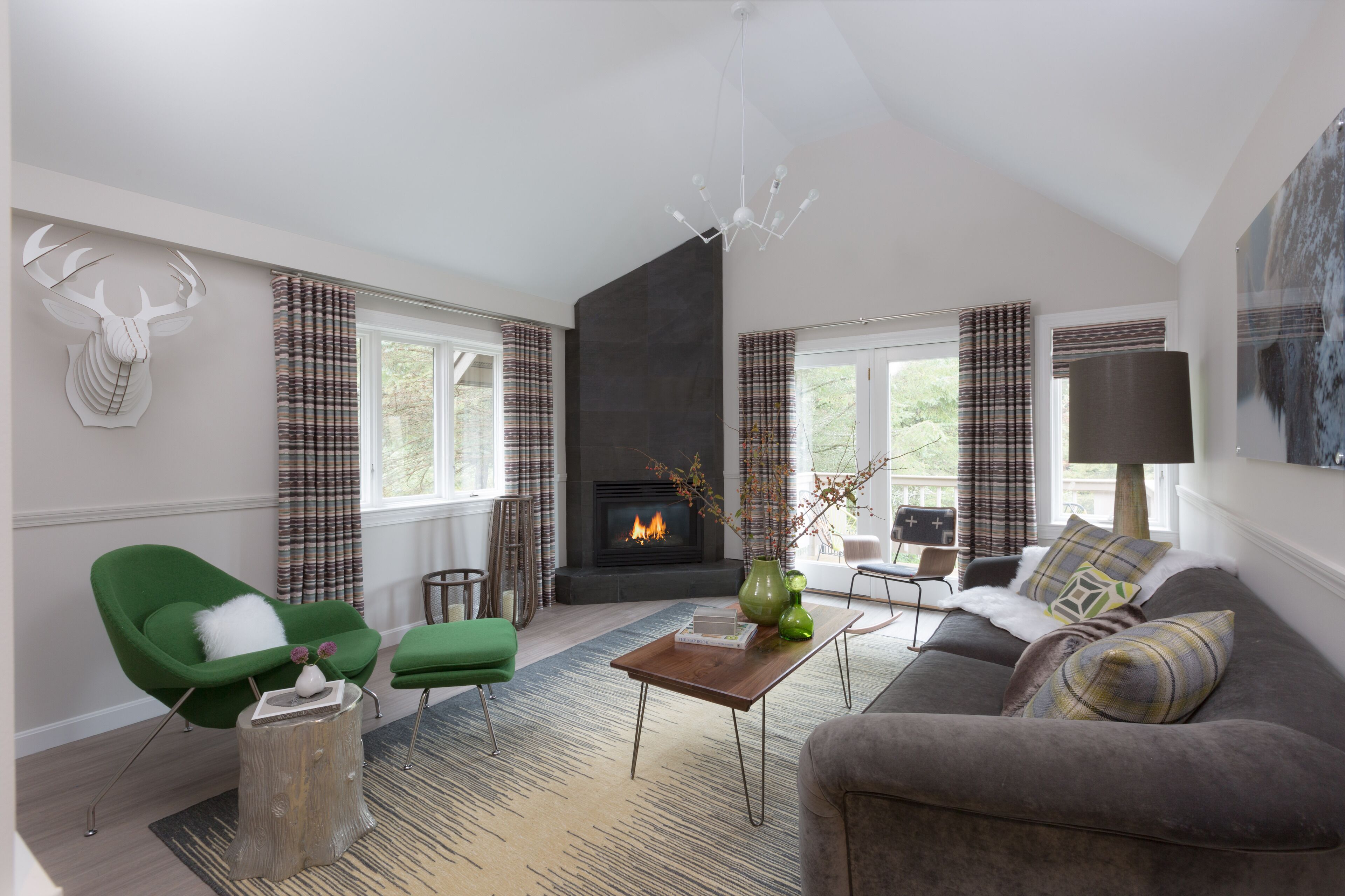 A modern living room with a fireplace, green and grey furniture, and a large window with curtains.