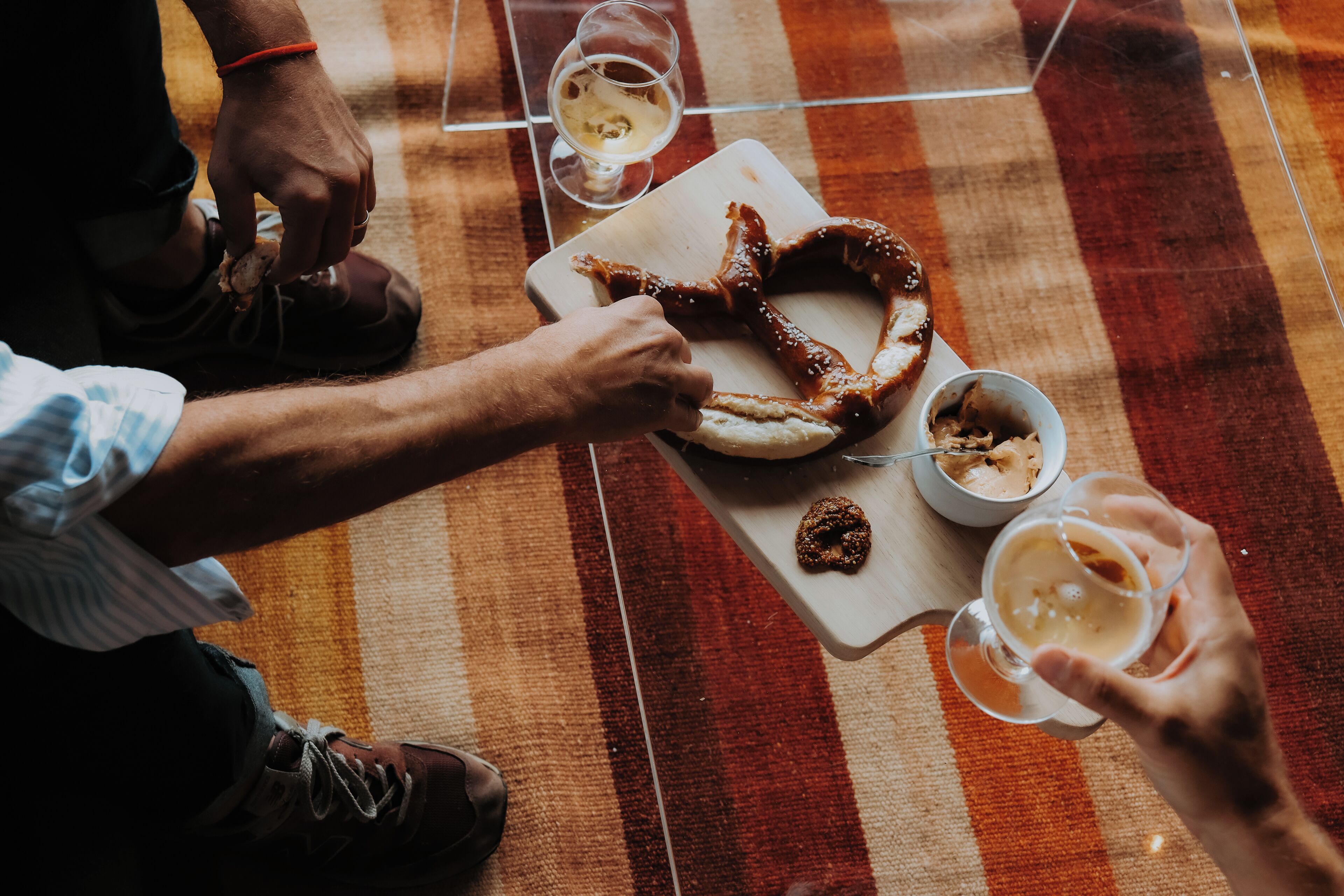 A dining table with a pretzel, a bowl of soup, and two glasses of beer.