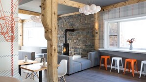 Un interior acogedor con chimenea de piedra, vigas de madera y una zona de estar con taburetes y sofá.