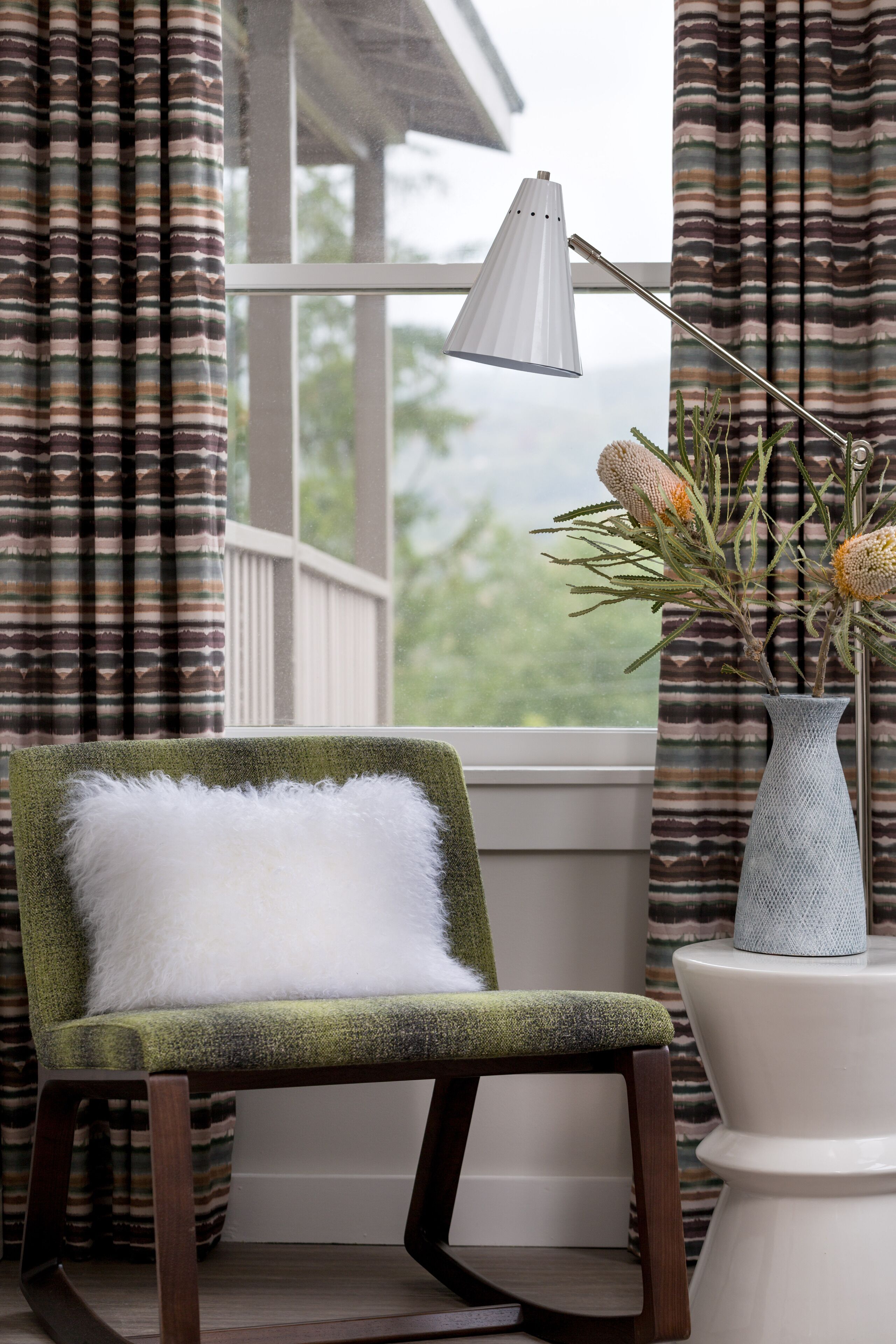 A chair with a white cushion, a vase with dried flowers, and a lamp on a windowsill.