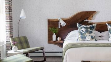 A modern hotel room with a wooden headboard, a green upholstered chair, a bedside table with a lamp, and a bed with white linens and blue patterned pillows.