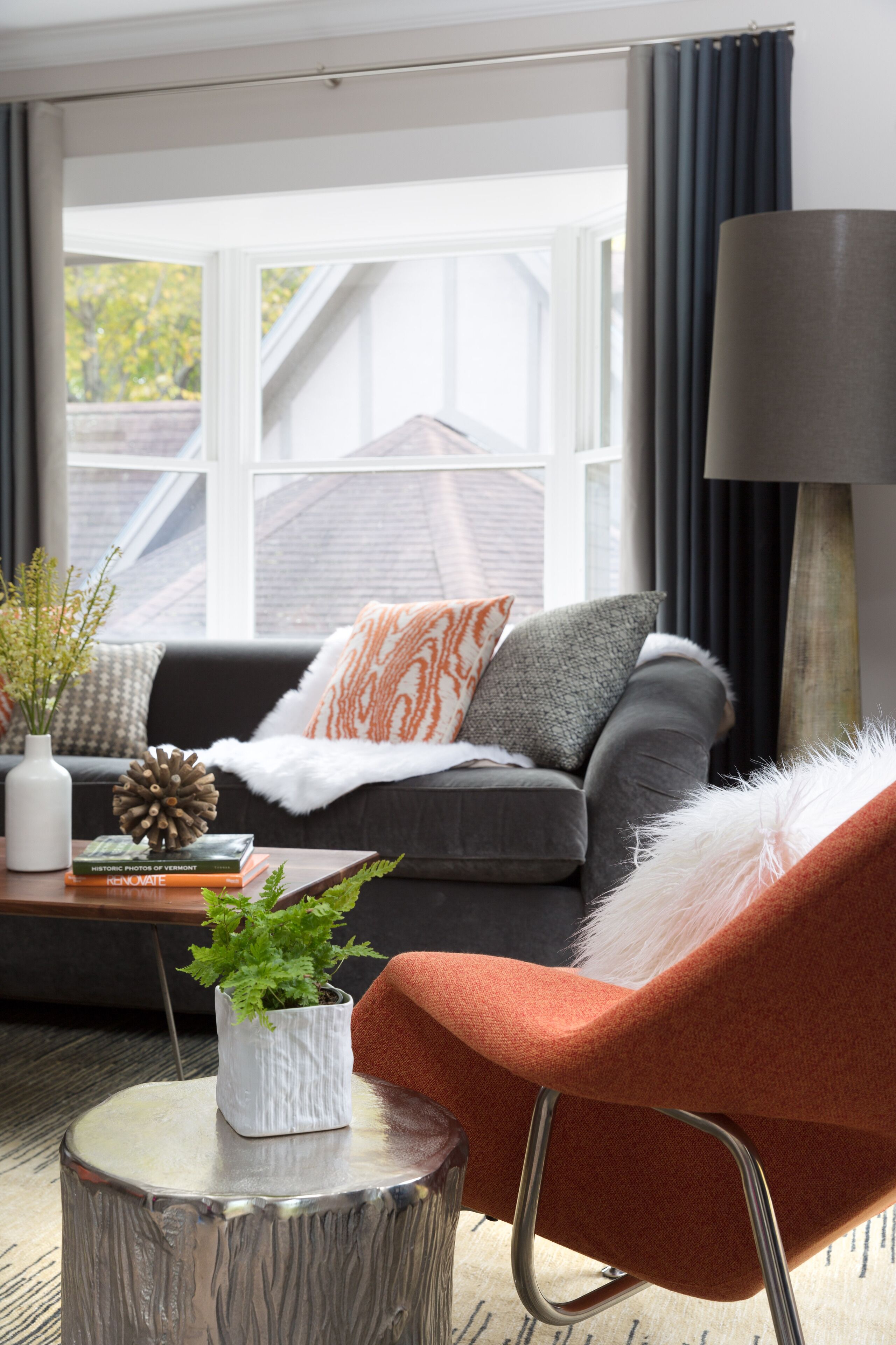 A living room with a grey sofa, orange armchair, and a coffee table with a plant and books.