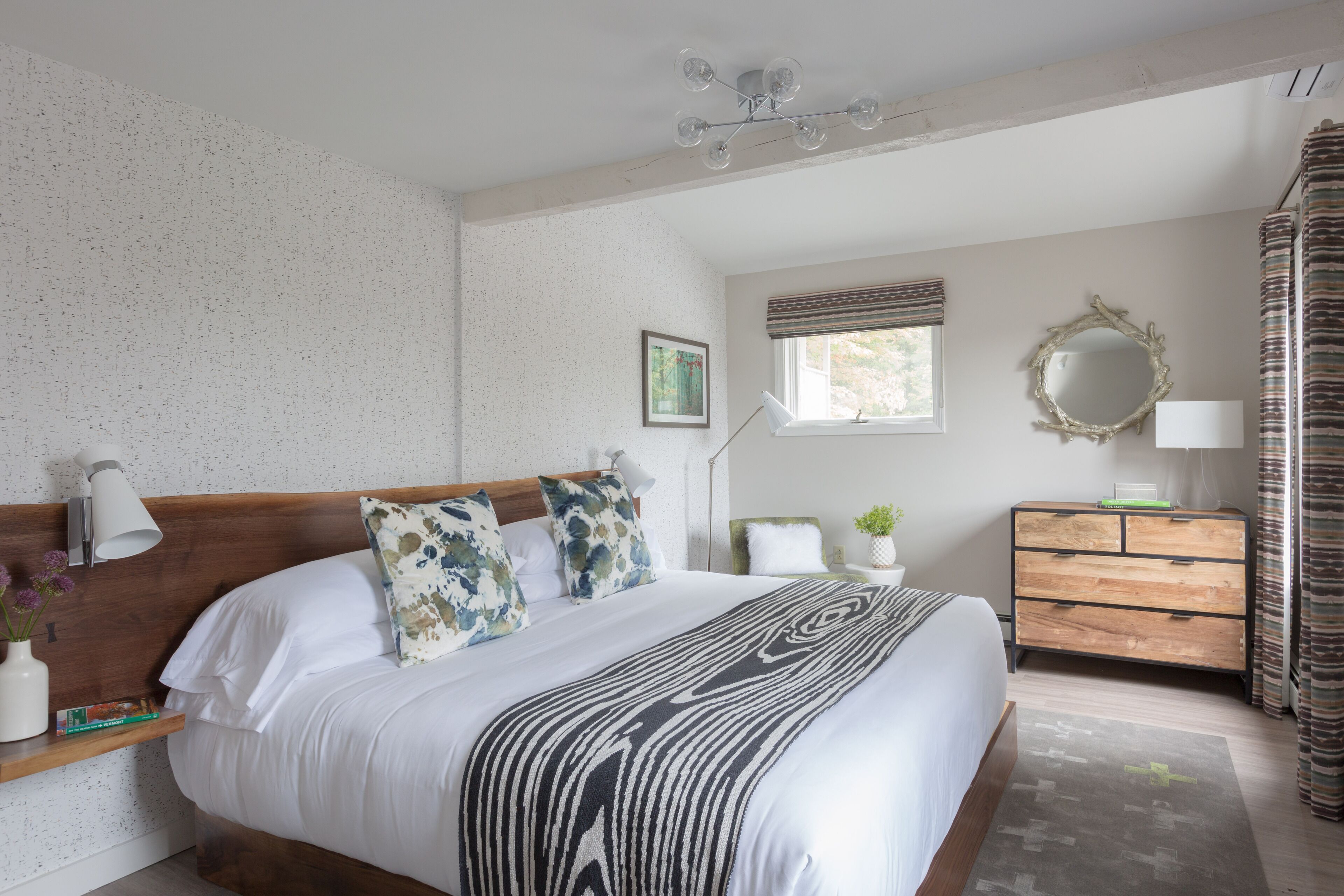 A neatly arranged bedroom with a large bed, bedside tables, a dresser, and a window with curtains.