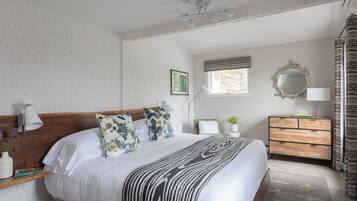 A neatly arranged bedroom with a large bed, bedside tables, a dresser, and a window with curtains.