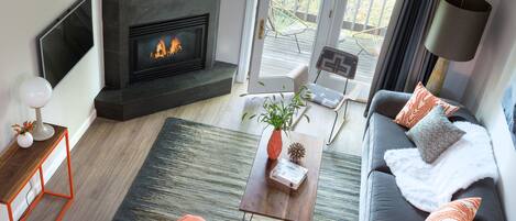A modern living room with a fireplace, a sofa, a coffee table, and orange chairs.
