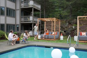 A pool area with a seating arrangement and a building in the background.
