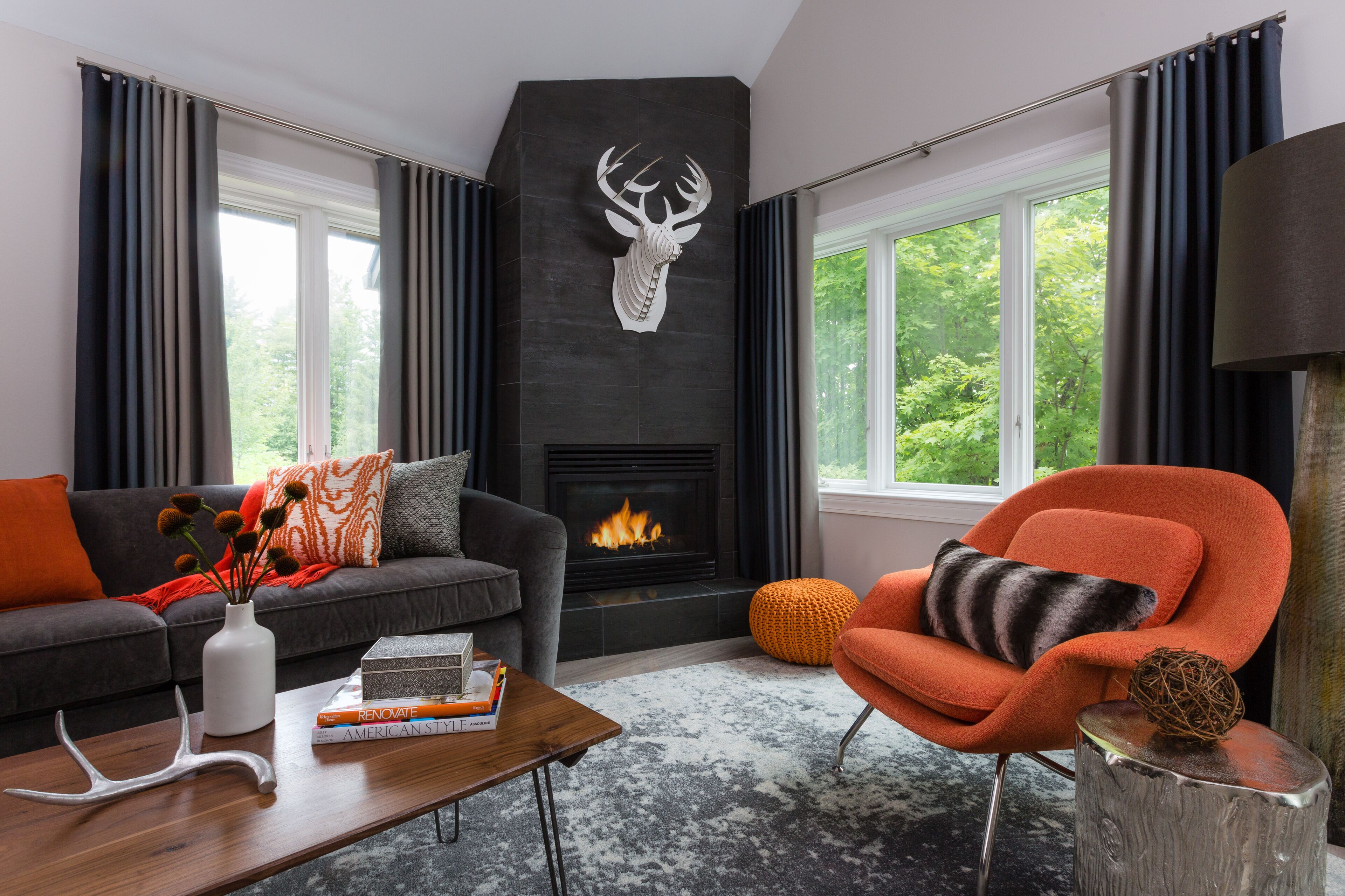 A modern living room with a fireplace, a sofa, an orange armchair, and a coffee table with books and a vase.