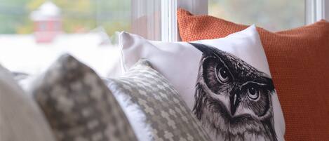 Asiento junto a la ventana con un cojín con diseño de lechuzas, un cojín estampado y un cojín naranja.