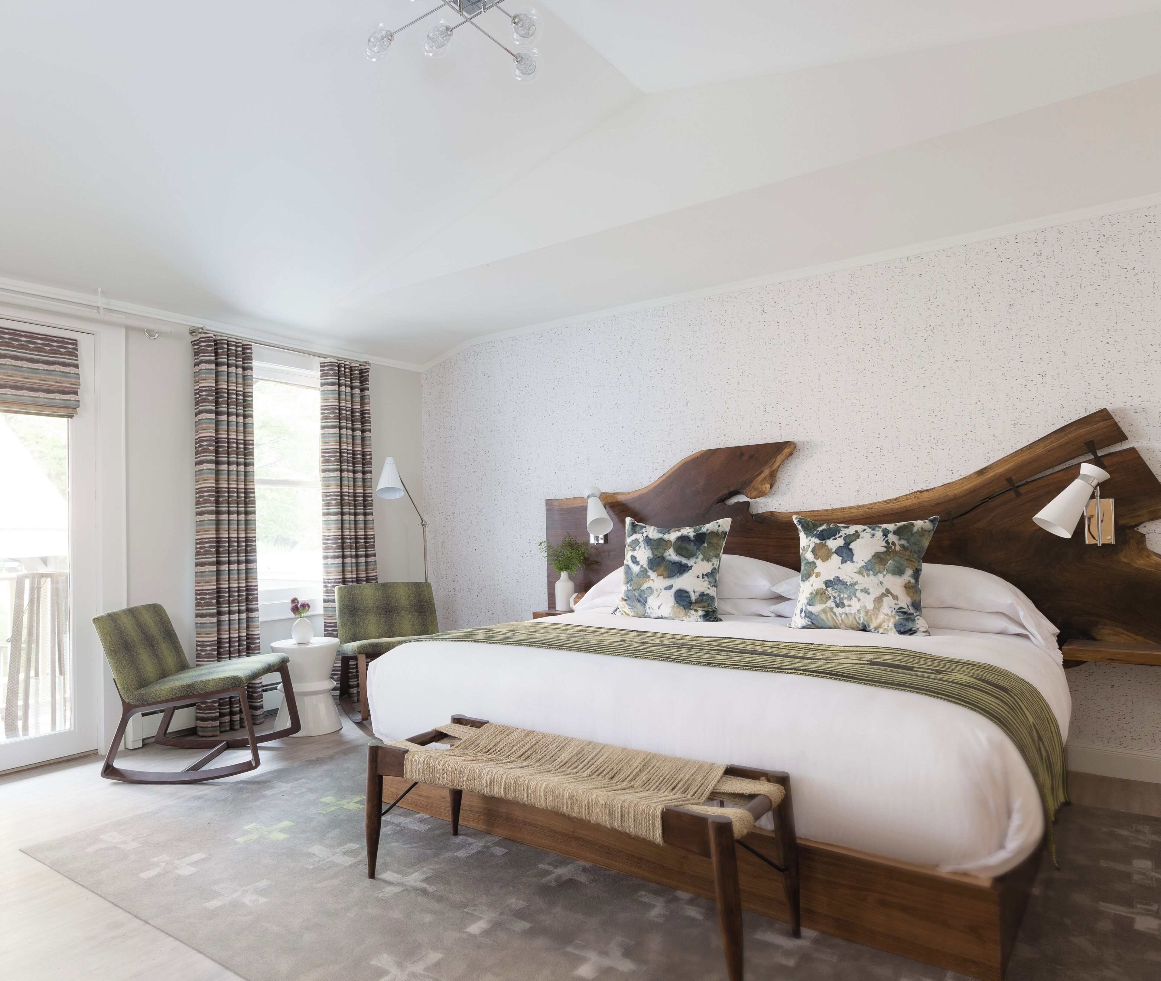 Une chambre à coucher moderne avec un grand lit, une tête de lit en bois, un fauteuil à bascule et une petite table de chevet avec une lampe.