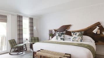 A modern bedroom with a large bed, a wooden headboard, a rocking chair, and a small side table with a lamp.