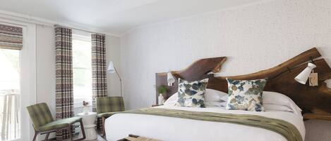 A modern bedroom with a large bed, a wooden headboard, a rocking chair, and a small side table with a lamp.