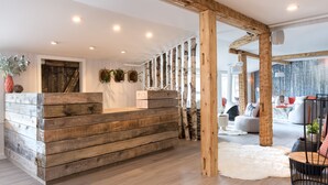 Un mostrador de recepción de madera con diseño rústico, una alfombra mullida blanca y un área de estar con un sofá moderno y una silla.