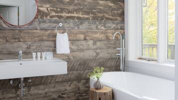 Un baño moderno con pared de madera, un lavamanos blanco, una bañera y un ventanal con vista a árboles.